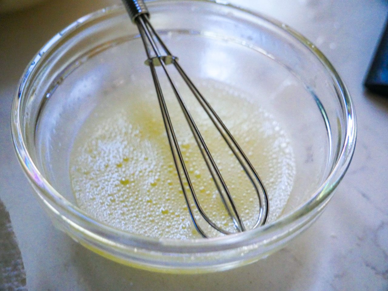 Egg whites with a mini whisk in a small bowl bubbling on a white countertop