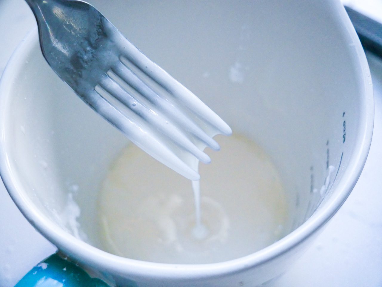 Elderflower glaze on a fork dripping into a liquid measuring cup