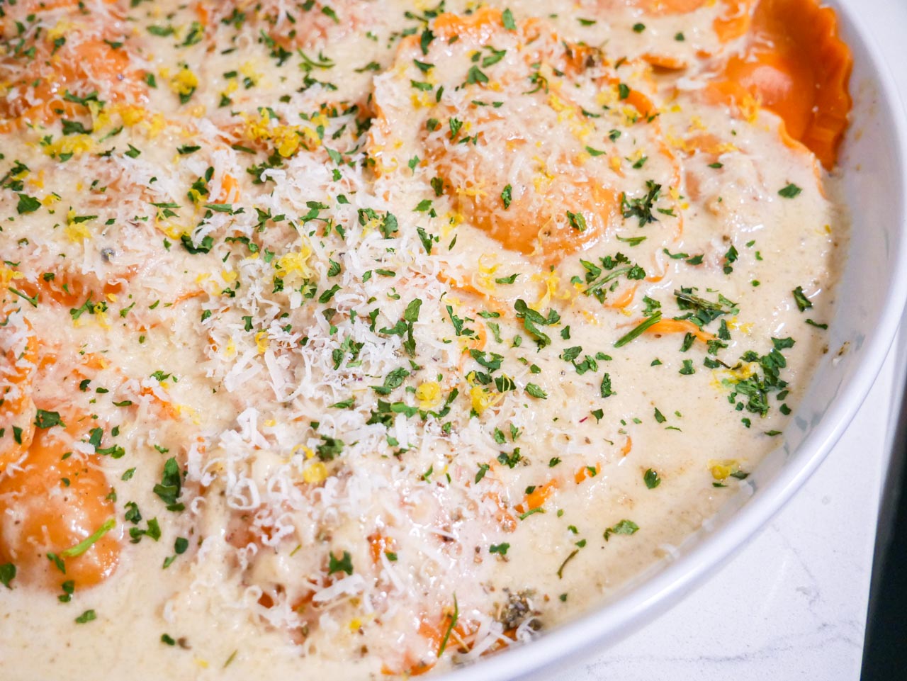 Creamy sage parmesan sauce on butternut squash ravioli in a white bowl on a white countertop.