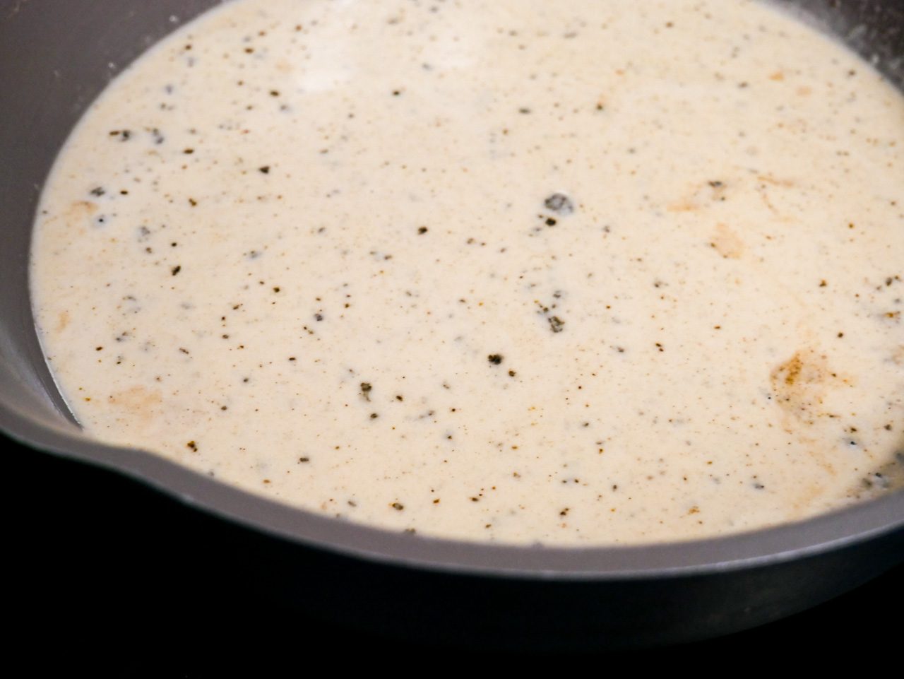 Creamy parmesan sauce in a gray, blue pan on a stovetop.