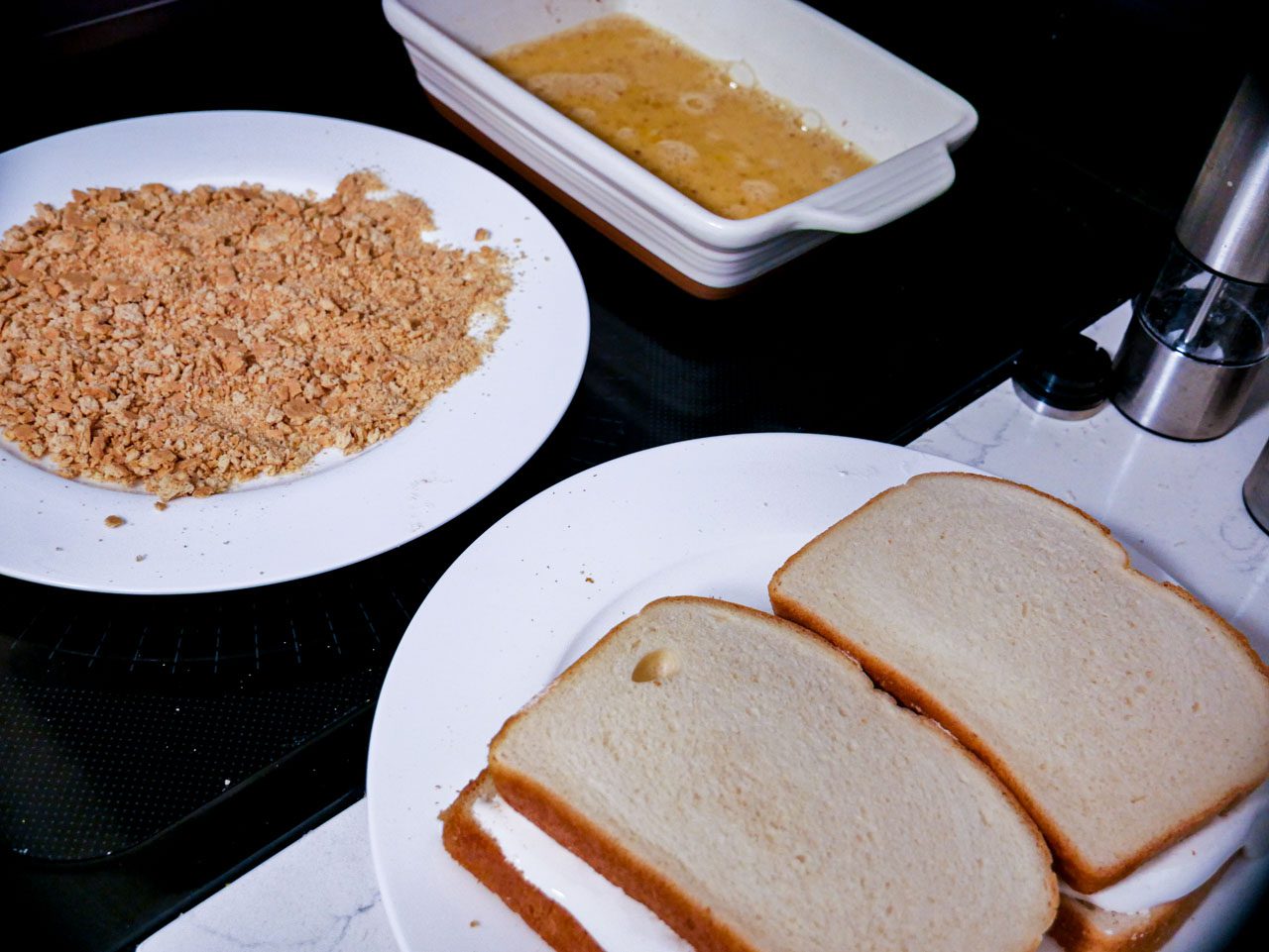 Egg wash in a dish, crushed graham cracker on a separate plate and prepared sandwiches ready to be breaded.