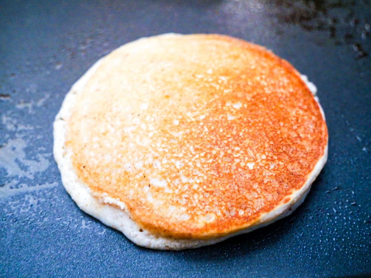 Single tiger nut flour pancakes on a black griddle golden brown.