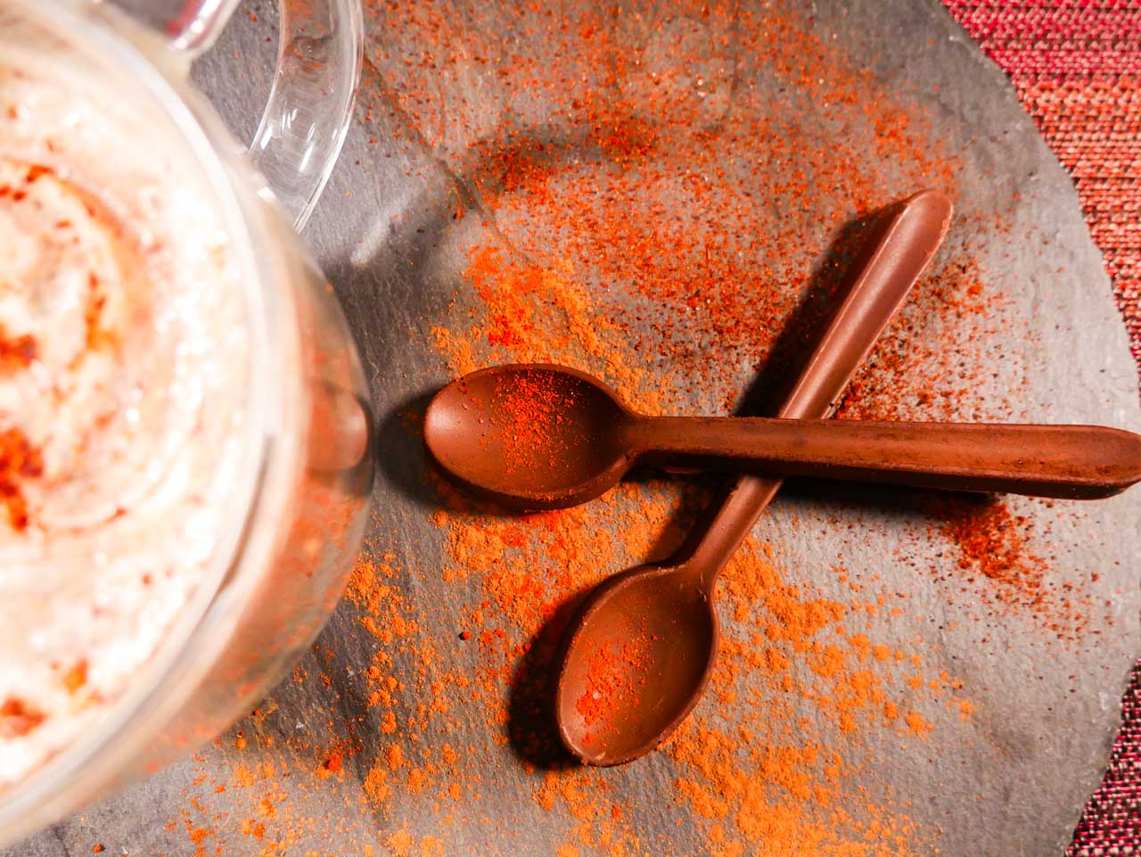 Mexican hot chocolate spoons next to a cup of hot chocolate with spices scattered all around. 