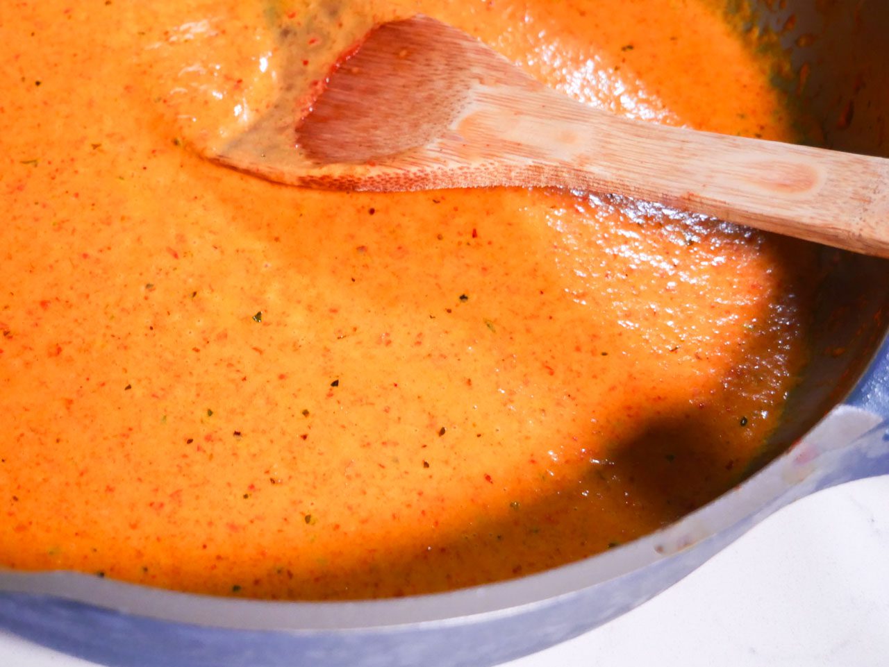 Roasted red pepper sauce in a blue pan with a wooden spoon in the middle