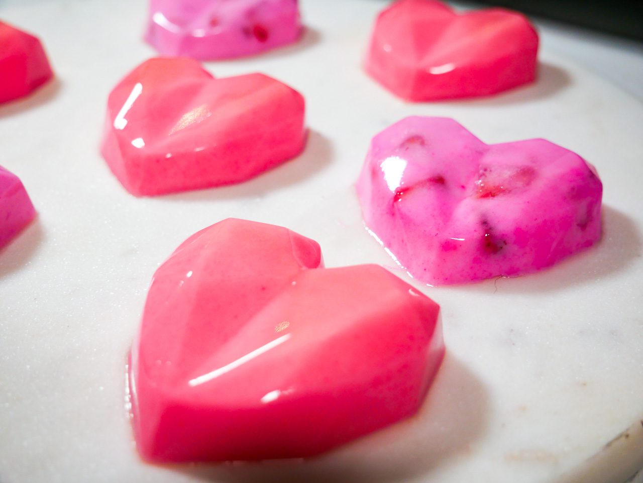 Heart shaped coconut jellies made with agar agar and chopped fruit on a white marble top. 