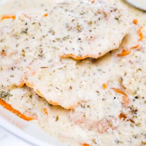 Creamy sage parmesan sauce over butternut squash ravioli in a white bowl on a countertop.